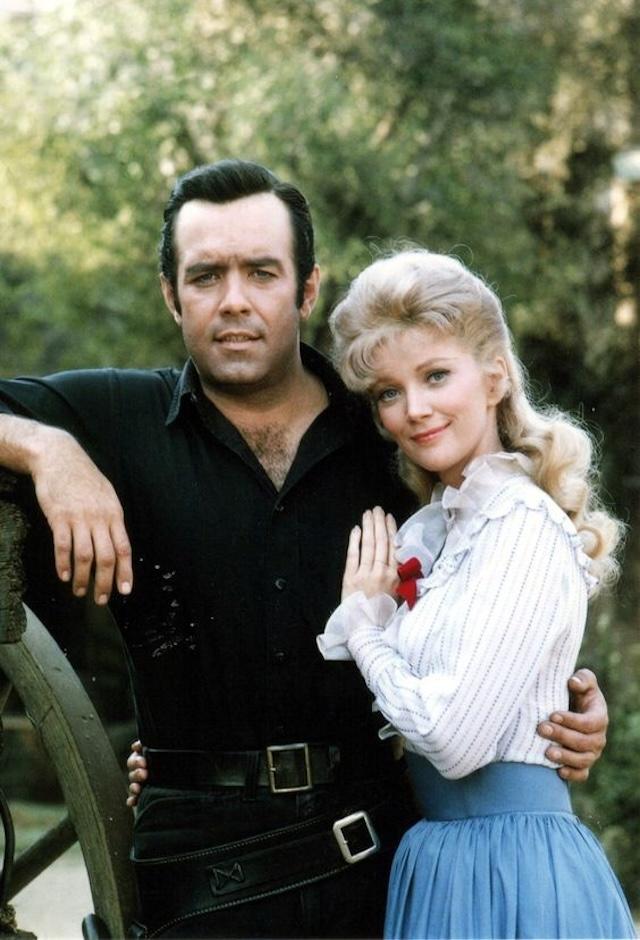 Prnell Roberts and Kathie Browne on the set of Bonanza, portraying Adam Cartwright and his love interest Laura Dayton, sharing a tender moment during the show's fifth season.
